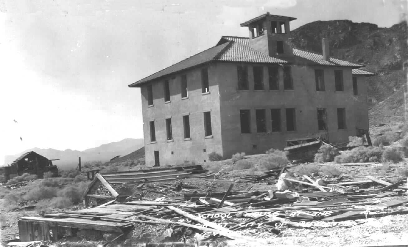 The abandoned three-storey Rhyolite school building standing intact above a field of collapsed timber