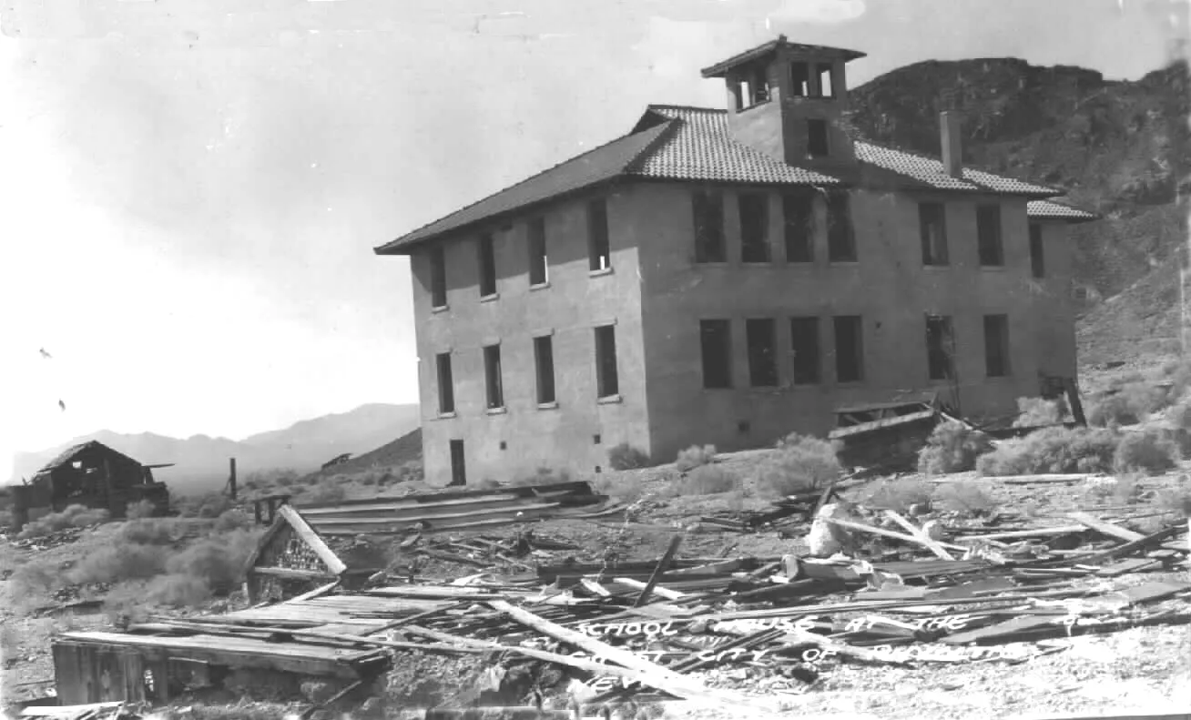 The abandoned three-storey Rhyolite school building standing intact above a field of collapsed timber