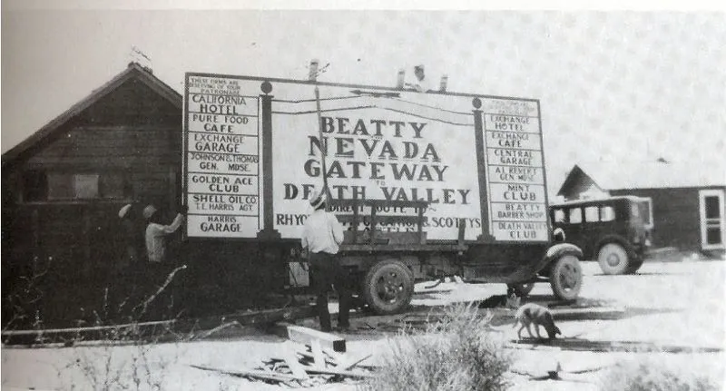 Men building a roadside billboard reading Beatty Nevada Gateway to Death Valley, listing the town's hotels, cafes and garages
